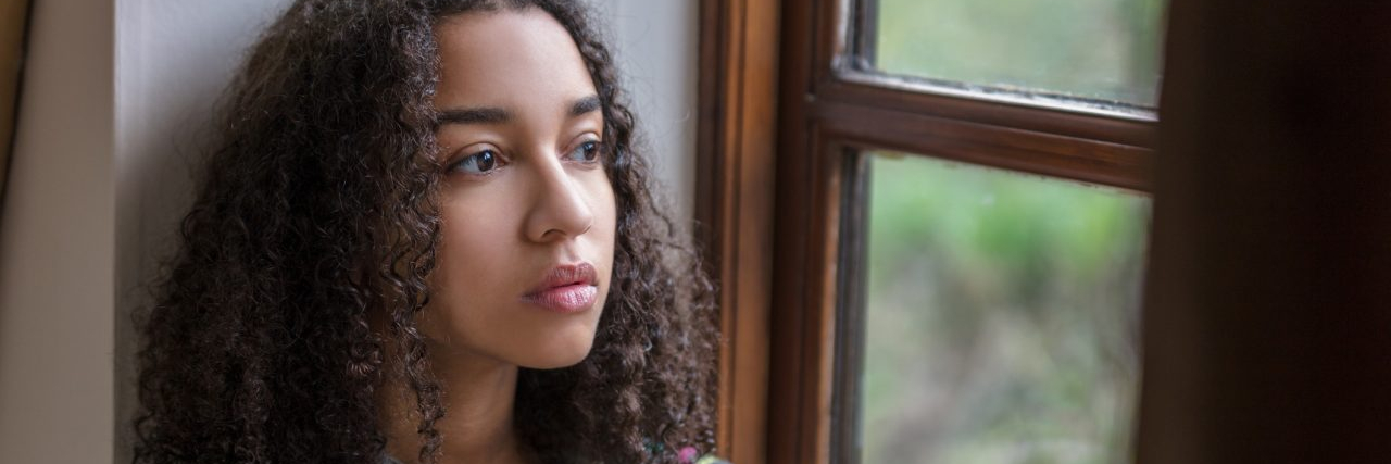 Beautiful mixed race teenager depressed or thoughtful looking out of a window