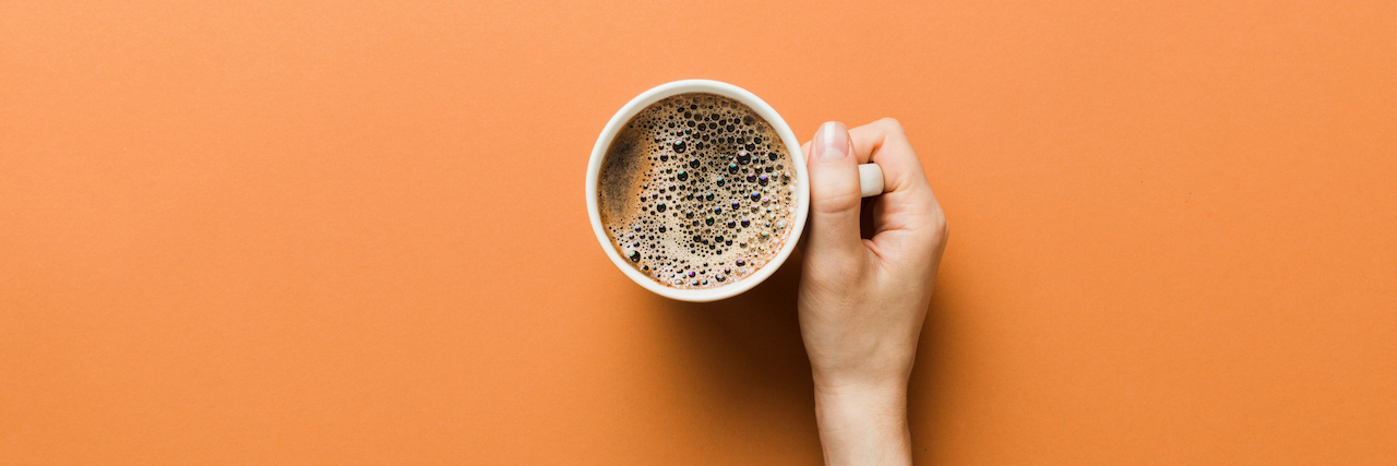 Woman's hand holding a cup of coffee on orange background.