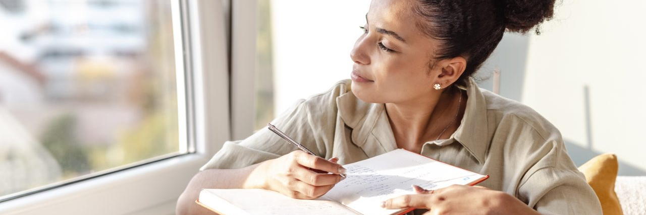 8 Tips for Creating Your Own Pain Scale A young woman is at home, she is sitting on the sofa in the living room and writing notes