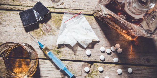 Overhead shot of hard drugs and alcohol on wooden table. Addiction concept