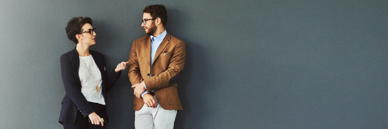 Two professionals leaning against a wall having a discussion