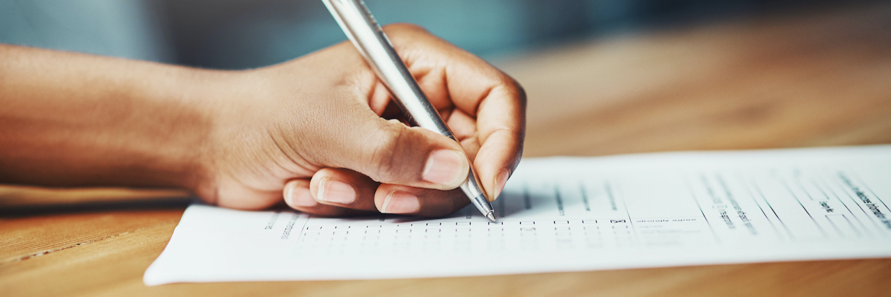 Can You Qualify for Disability Benefits With ADHD? Close up of a hand holding pen and filling out paperwork at a desk