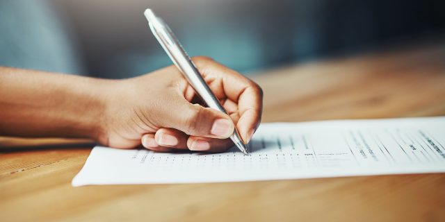 Can You Qualify for Disability Benefits With ADHD? Close up of a hand holding pen and filling out paperwork at a desk