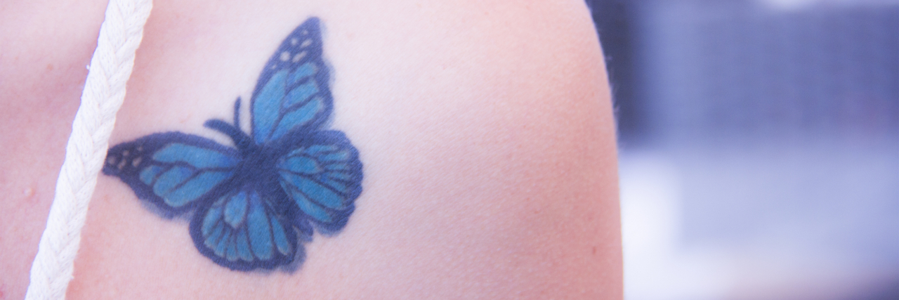 A blue butterfly tattoo on the front of a person's shoulder.
