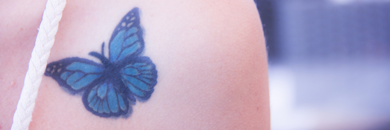 What Does a Butterfly Tattoo Mean in Mental Health? A blue butterfly tattoo on the front of a person's shoulder.