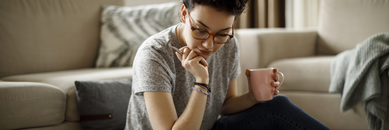 Is OCD A Neurodivergent Condition? A woman sitting on the floor looking at a laptop with a mug in hand.