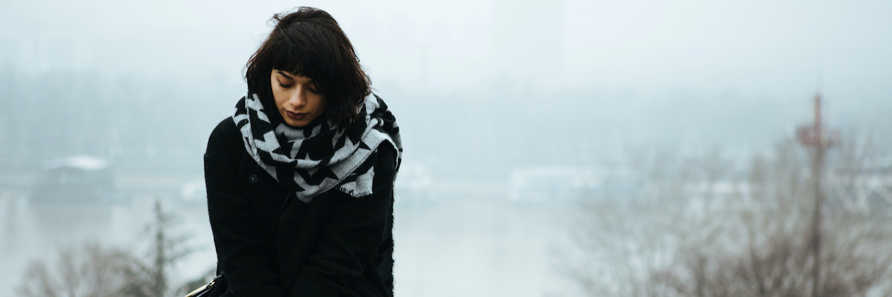 Exploring the Connection Between PMDD and ADHD Woman sitting alone on a ledge with river and trees behind her