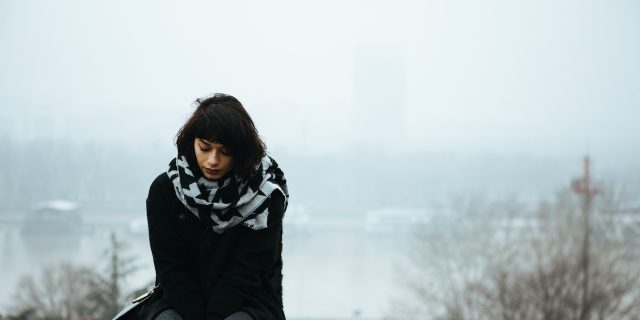 Exploring the Connection Between PMDD and ADHD Woman sitting alone on a ledge with river and trees behind her
