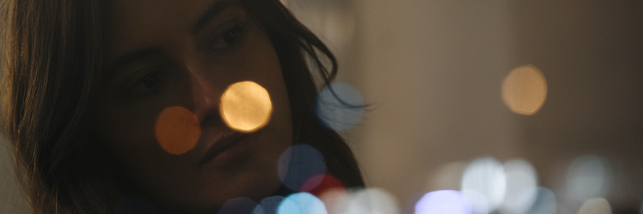 Woman looking out of window with lights blurred in reflection