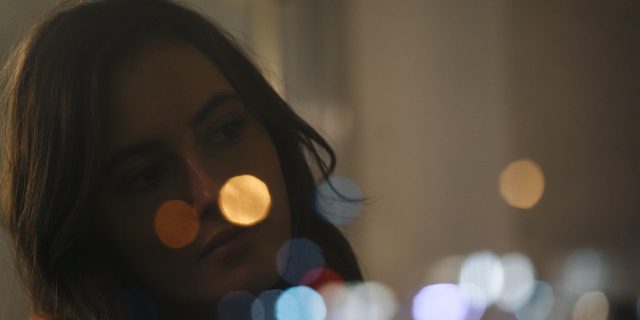 Woman looking out of window with lights blurred in reflection