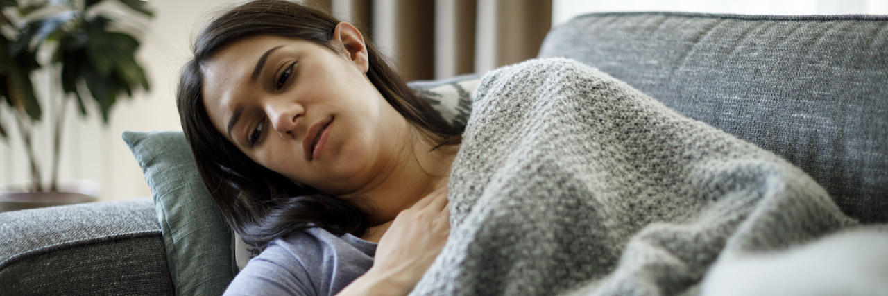Why Migraine Causes Nausea Lethargic woman laying on couch with blanket on her