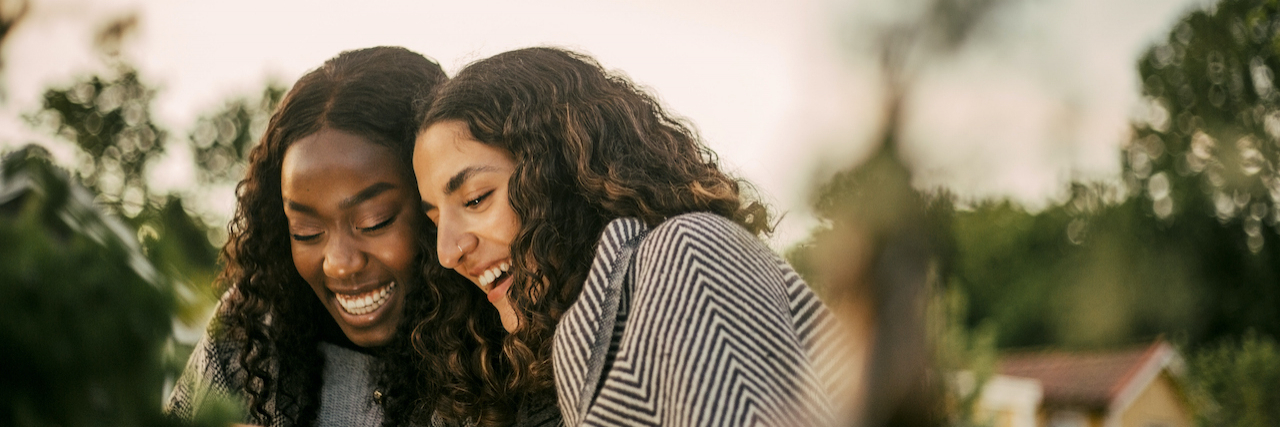 Is Epilepsy Contagious? Debunking Myths and Misconceptions Cheerful friends with heads together looking at phone outside. Women of color