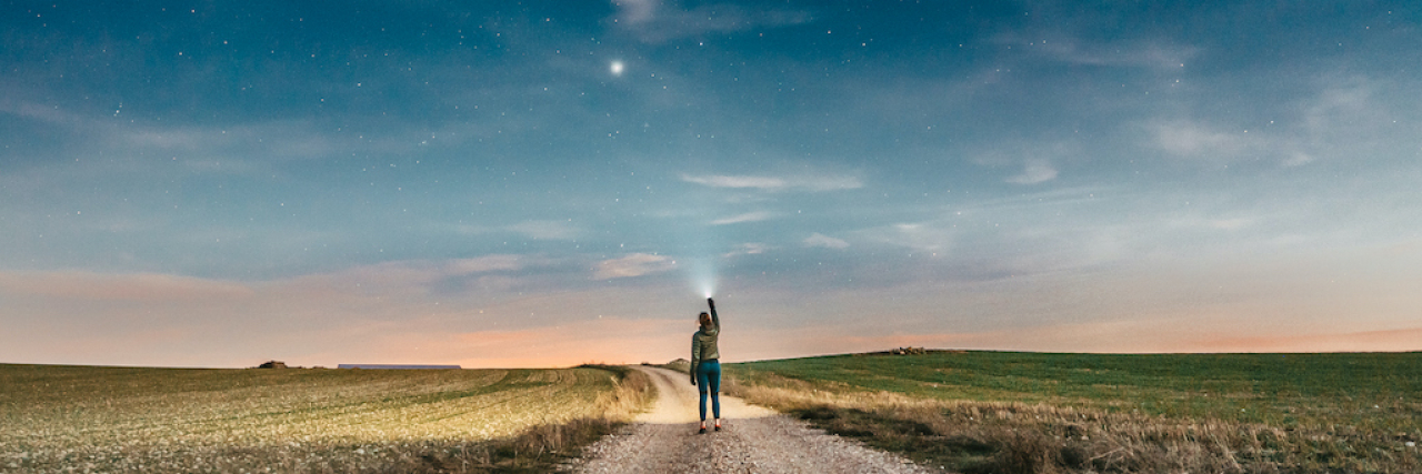 If You’re Feeling Lost in Life Woman pointing a lantern up while walking on a country road at night with the sky full of stars