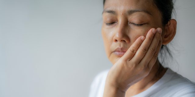 The Connection Between TMJ and Migraine Woman holding her jaw