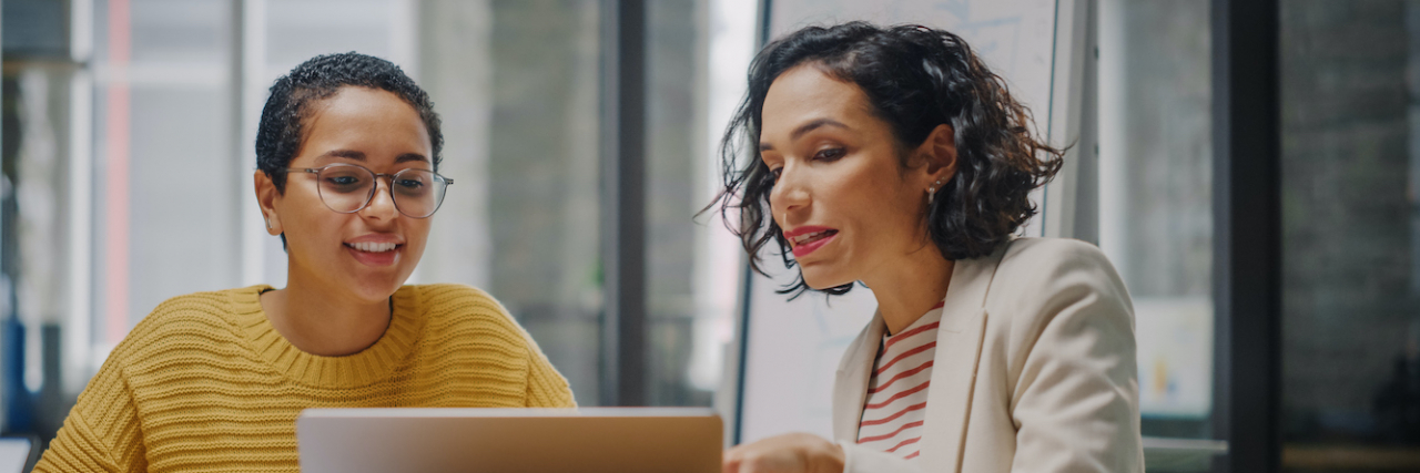 Two women of color at work having a discussion by a laptop
