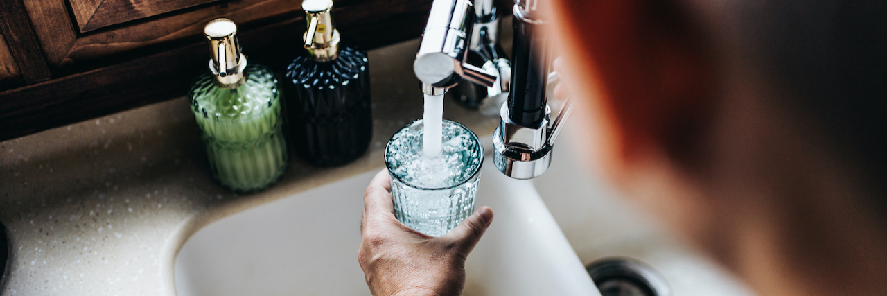 The Role Dehydration Plays in Migraine Over the shoulder view of man filling a glass of water from the kitchen