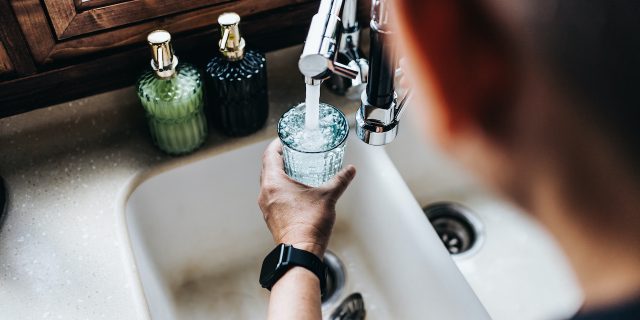 The Role Dehydration Plays in Migraine Over the shoulder view of man filling a glass of water from the kitchen