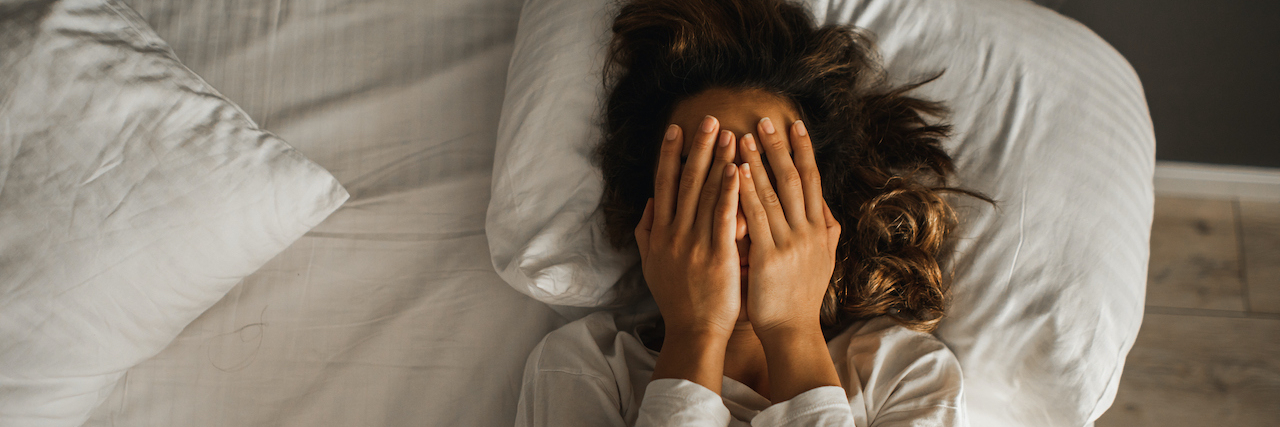 Why Depression Makes You Tired Woman with hands over face in bed.