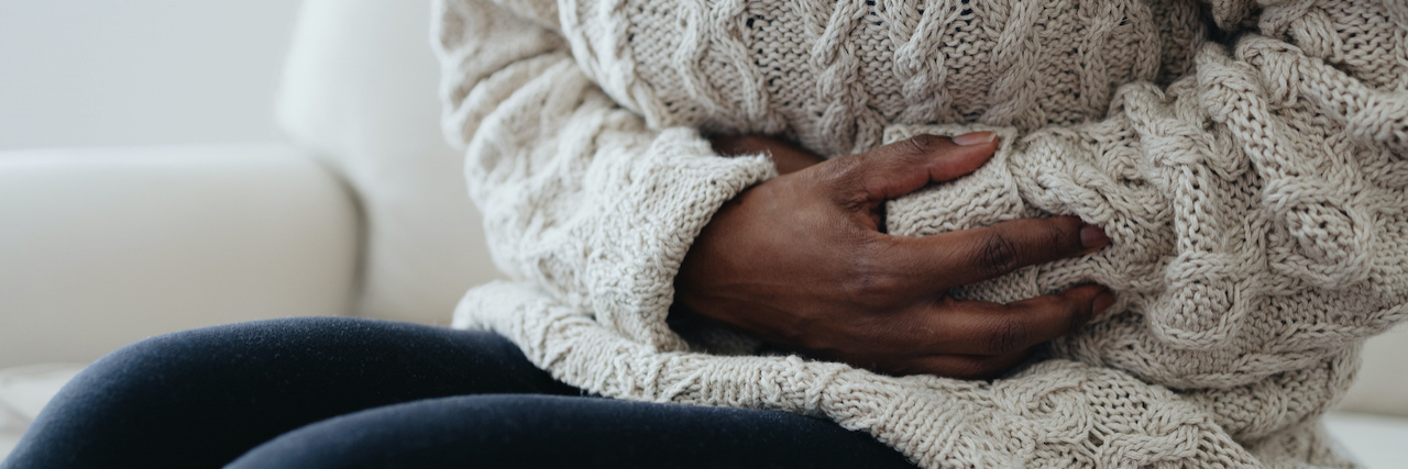 The Link Between Migraine, Diarrhea, and Gastrointestinal Issues Close-up of Black woman sitting on sofa holding her abdomen in pain
