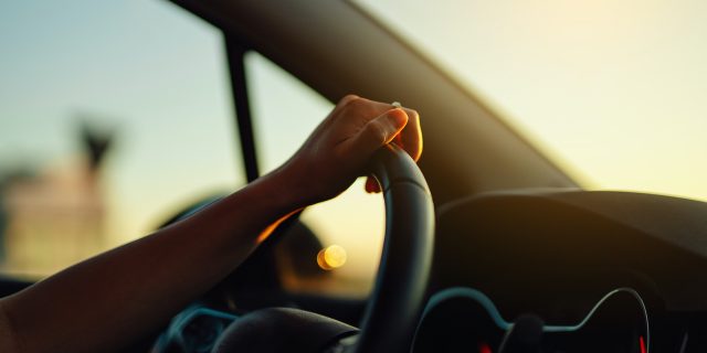 Close up of hand holding steering wheel in a car during a drive