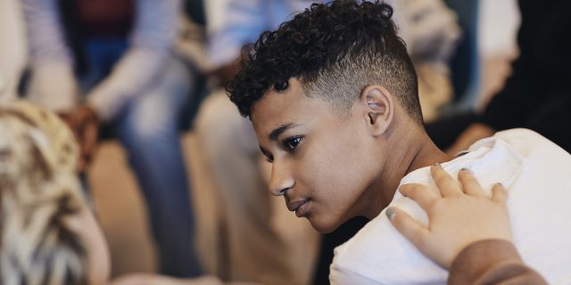 Signs of Depression in Teens: What to Look For Teenage boy of color with someone's hand on his shoulder in support