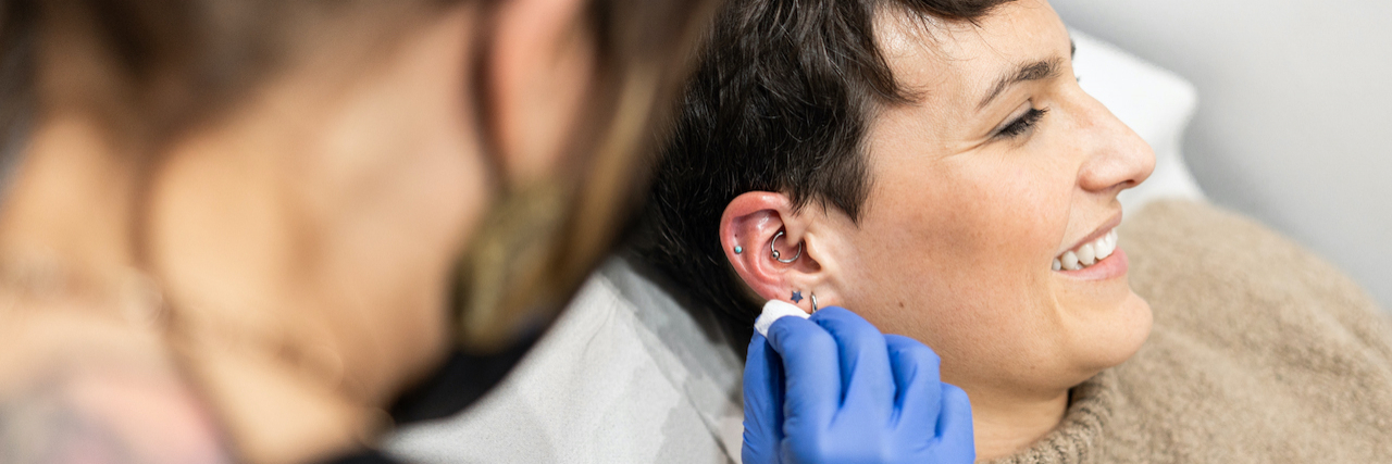 A piercer cleaning client's ear in preparation for piercing