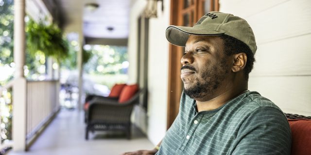 Portrait of Black U.S. military veteran on front porch of suburban home