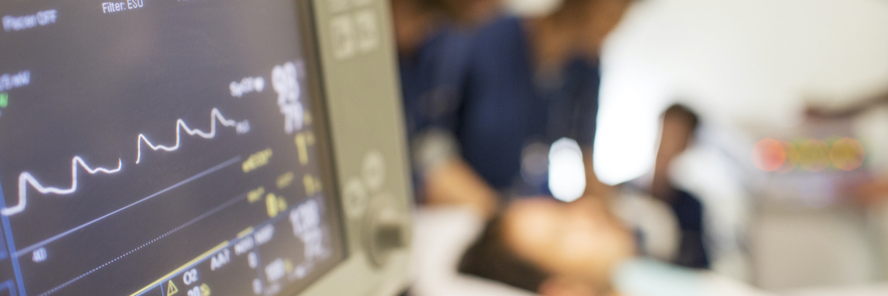 Close up of vitals monitor in hospital with doctors and patient blurred in background