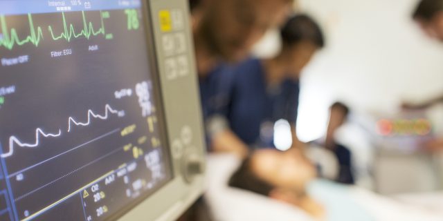 Close up of vitals monitor in hospital with doctors and patient blurred in background