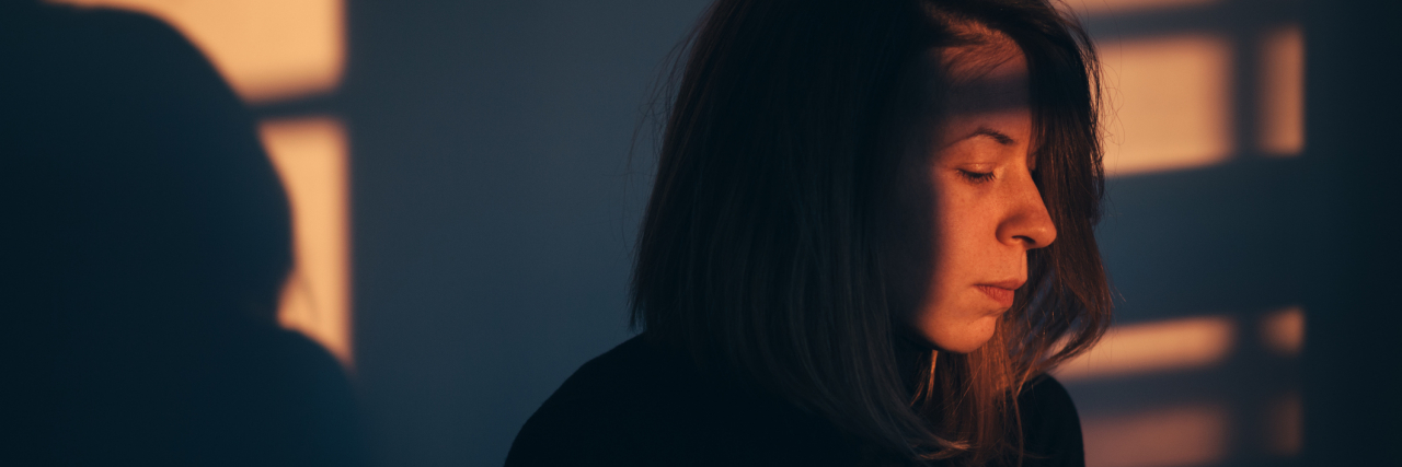 What 'Relapse' Means in Mental Health Woman standing in the shadows inside a room during sunset .