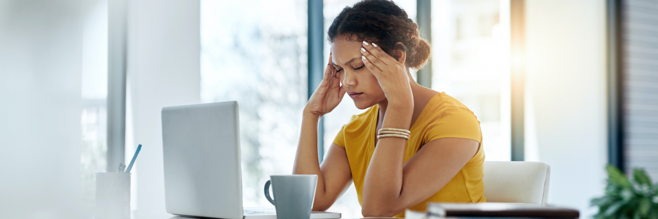 Can a Migraine Last a Week? Understanding Migraine Duration Woman of color holding her head in front of a desk