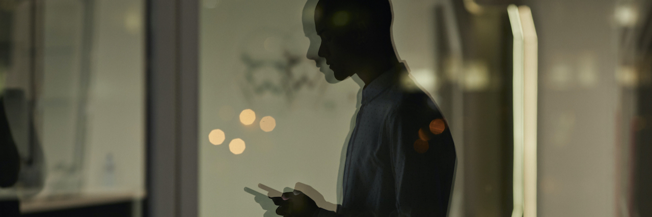 Blurred reflection of person checking phone inside office at night