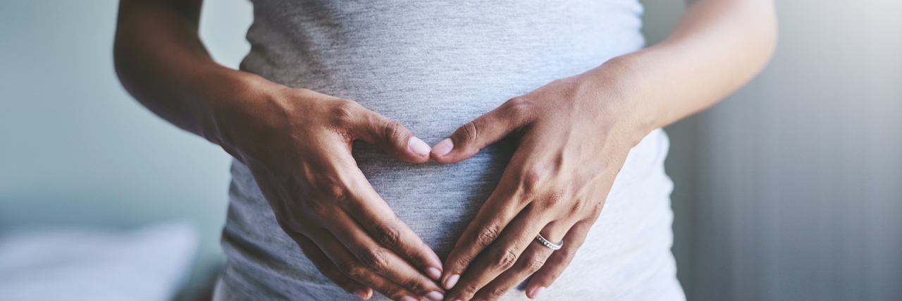 Cropped shot of a pregnant woman of color holding her hands in heart shape over her belly