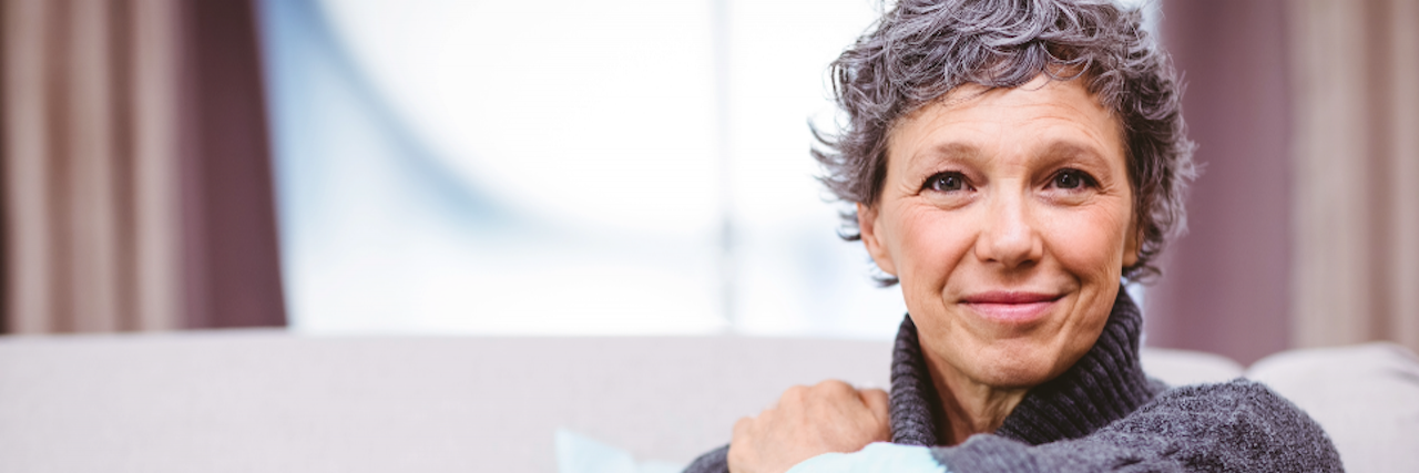 An Ever-Changing Journey: Life With Relapsed/Refractory AML Person sitting on a couch with their left hand on their right shoulder and knee up.