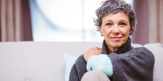 An Ever-Changing Journey: Life With Relapsed/Refractory AML Person sitting on a couch with their left hand on their right shoulder and knee up.