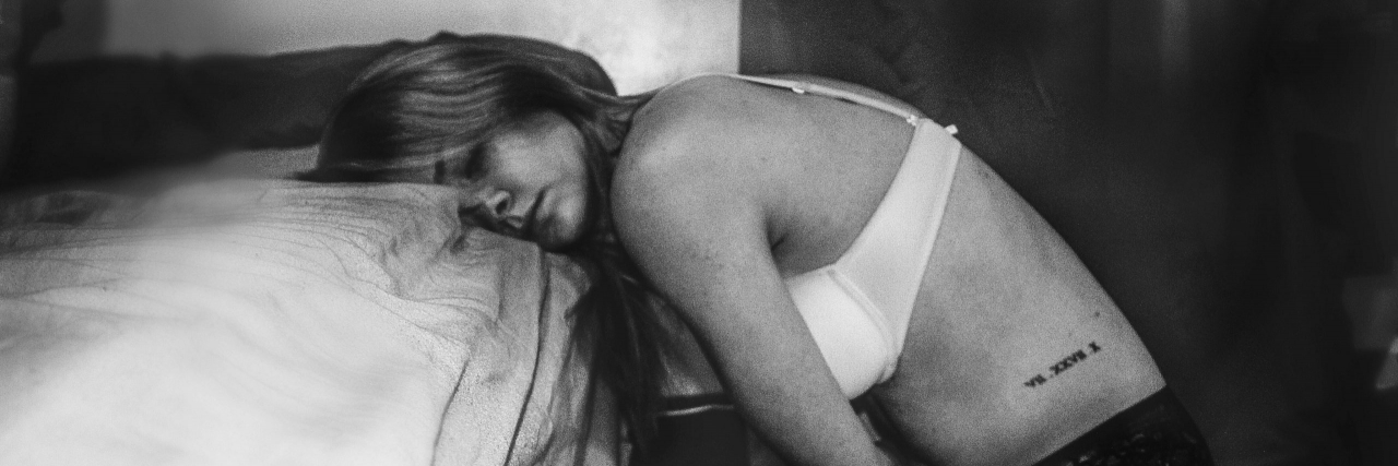 Black and white photo of woman leaning over bed as if in pain