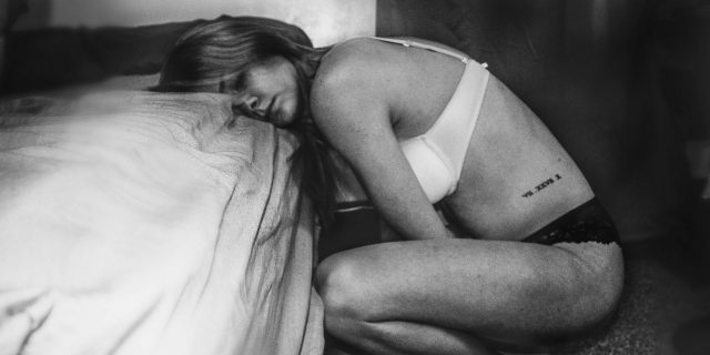 Black and white photo of woman leaning over bed as if in pain
