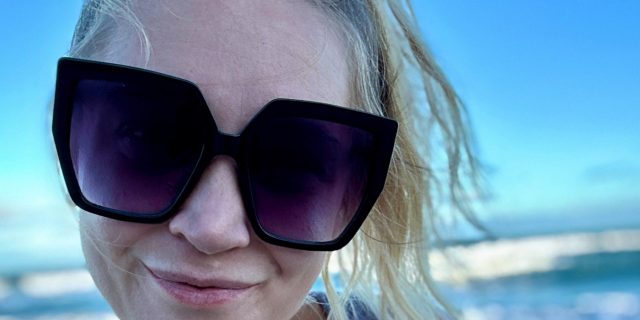 Contributor, a woman with blonde hair wearing sunglasses, outside with sunset behind her
