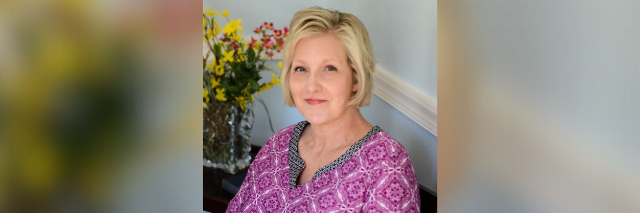 It's Time to Put Patients Over Profit Contributor seated at home with flowers behind her