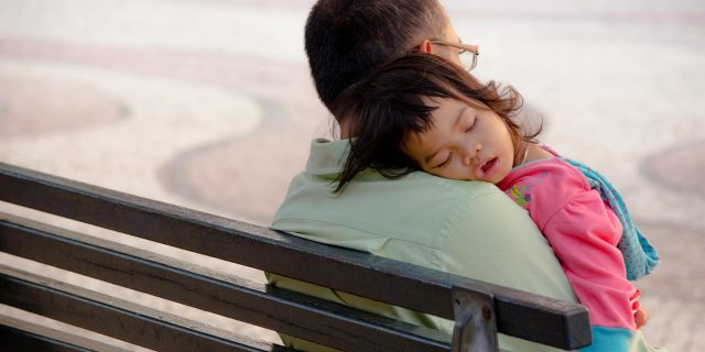 child sleeping on dad on a bench