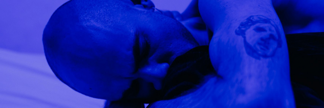 person with migraine in dark lit blue room