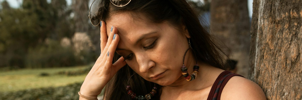 Hidden Migraine Triggers Person with headache outside by a tree