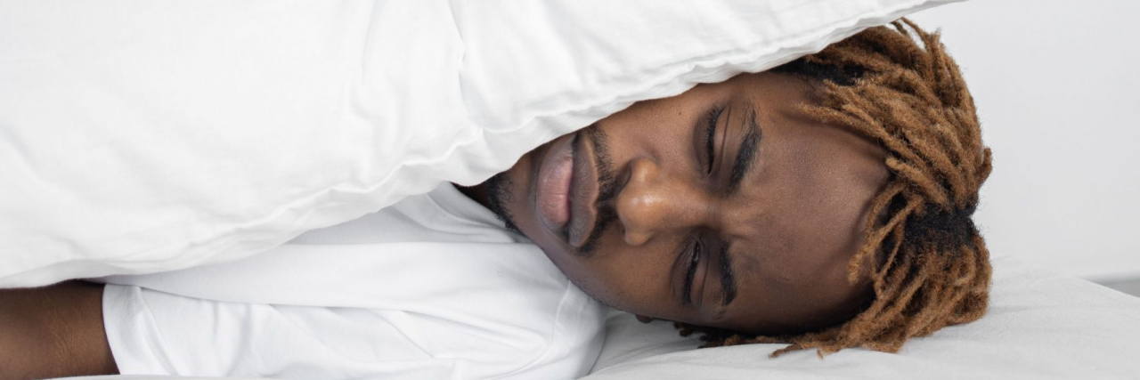 sleeping person covering their ears with a pillow