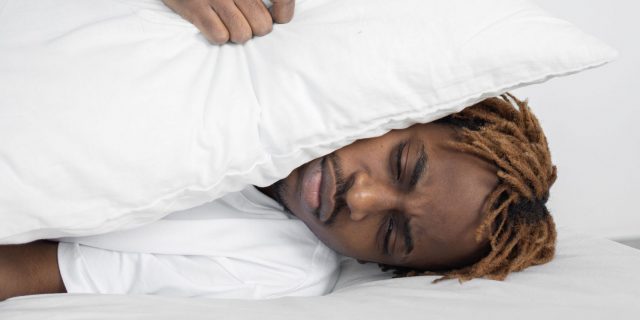 sleeping person covering their ears with a pillow